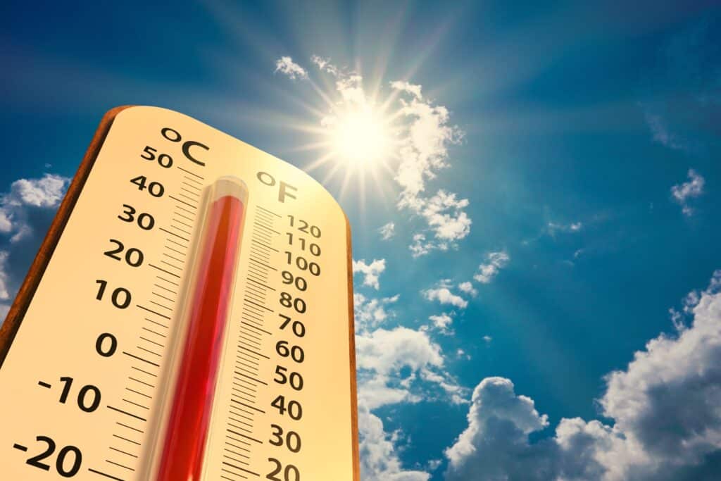 Thermometer with high reading with sun shining in background.